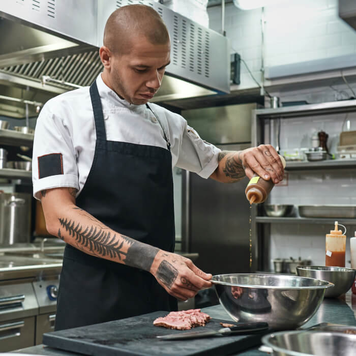 Küchenchef (Boss) bei der Arbeit. Er kippt gerade etwas Öl mit in das Gericht in die Pfanne.